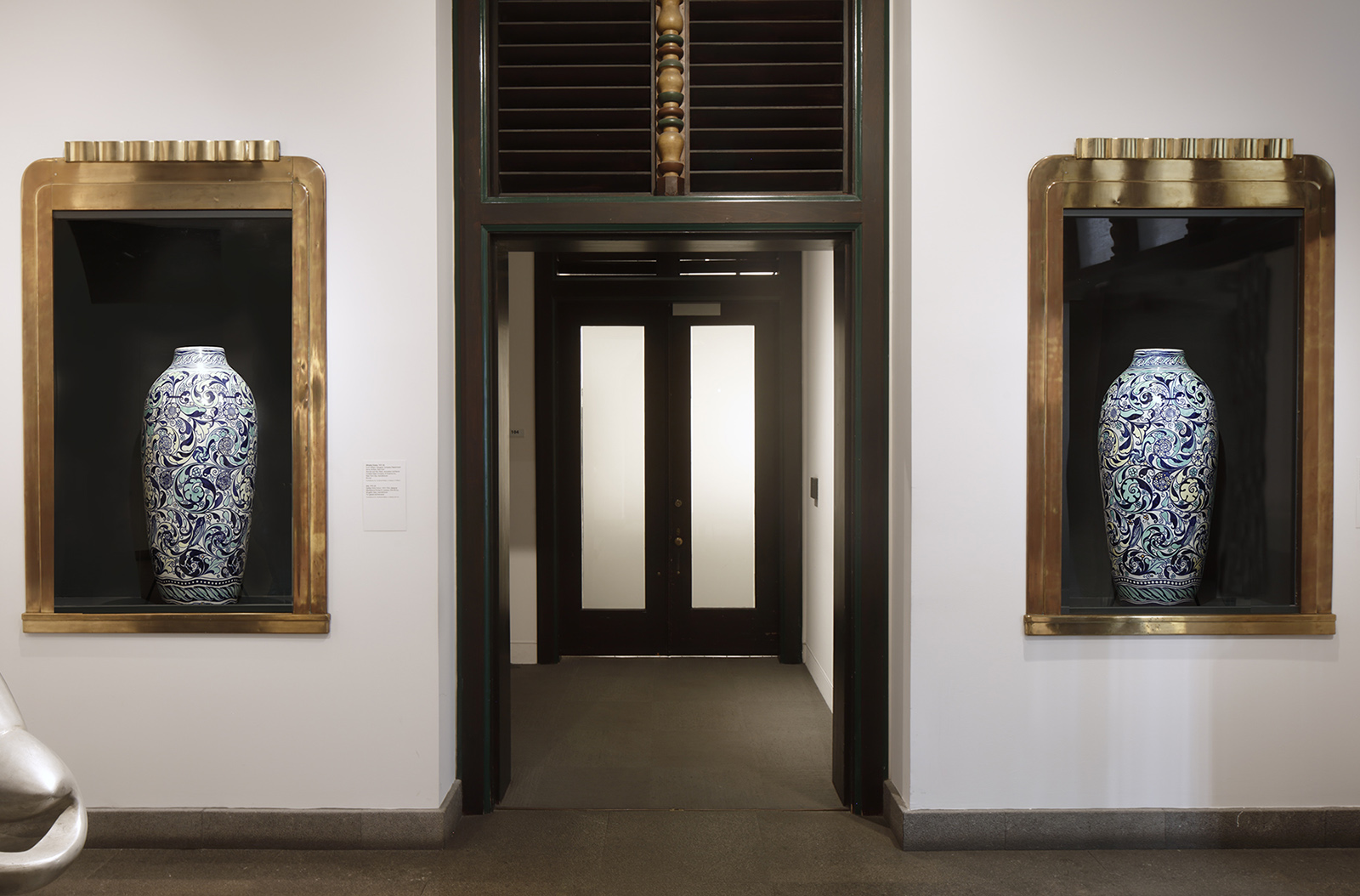 Interior room looking into another room with two display cases holding ceramic vases on either side of the doorway.
